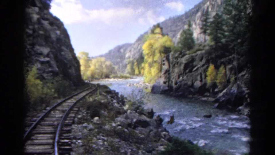 Colorado train-window view from 1967, with track, river, rocky slopes, evergreens, and yellow foliage visible ahead.