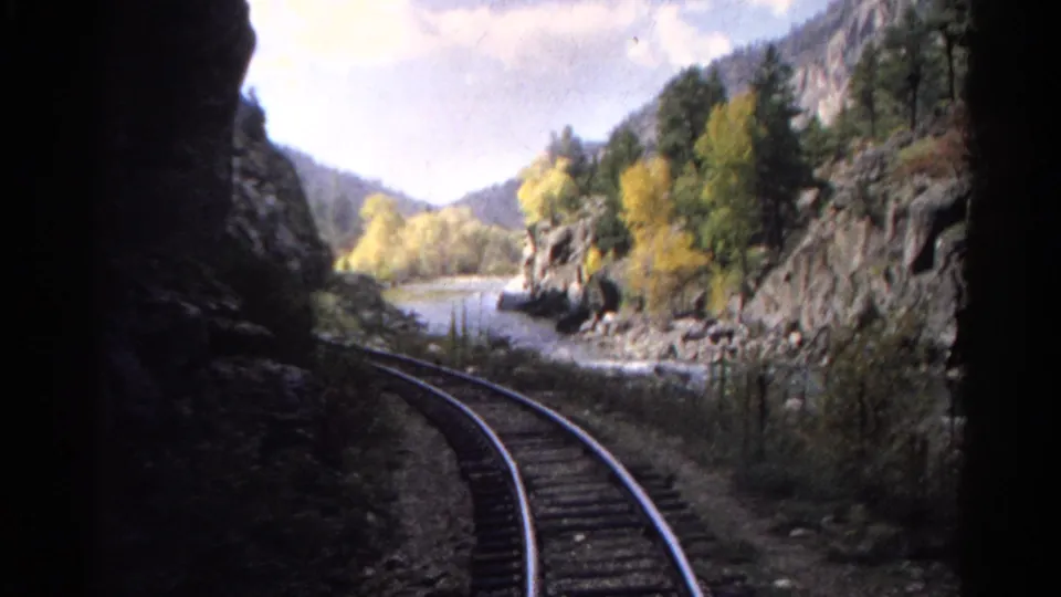 1967 Colorado 8mm frame with railroad tracks curving along the riverbank below rocky cliffs and autumn trees.