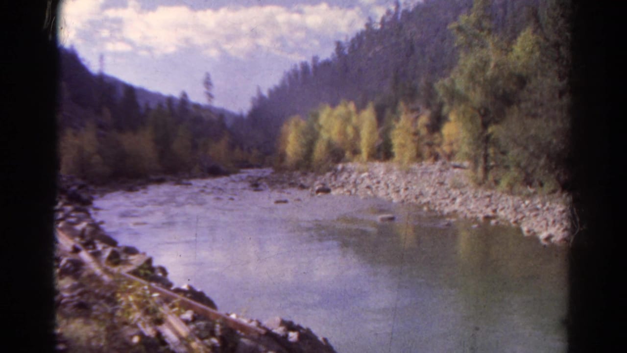 1967 Colorado 8mm view of a river curving through a forested mountain valley, seen from a moving train.
