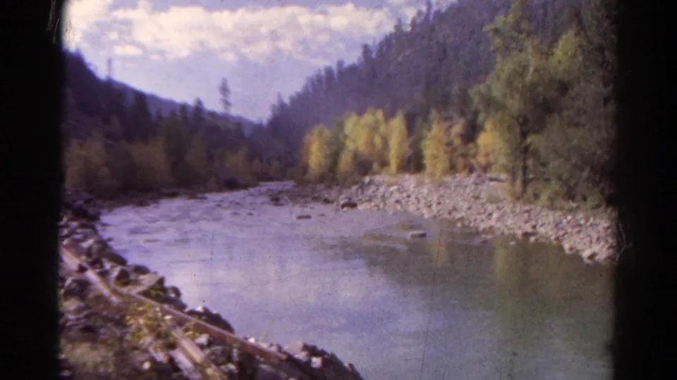1967 Colorado 8mm view of a river curving through a forested mountain valley, seen from a moving train.