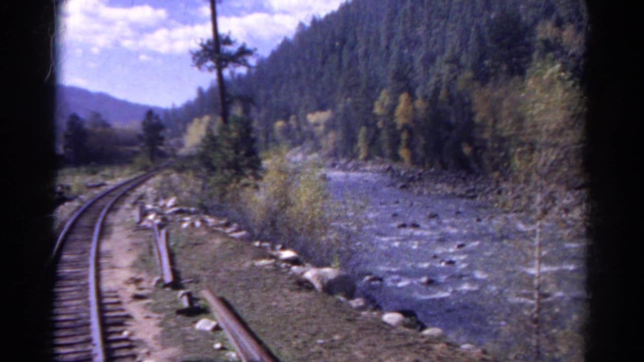 Railway tracks and a river curve through a forested mountain landscape.