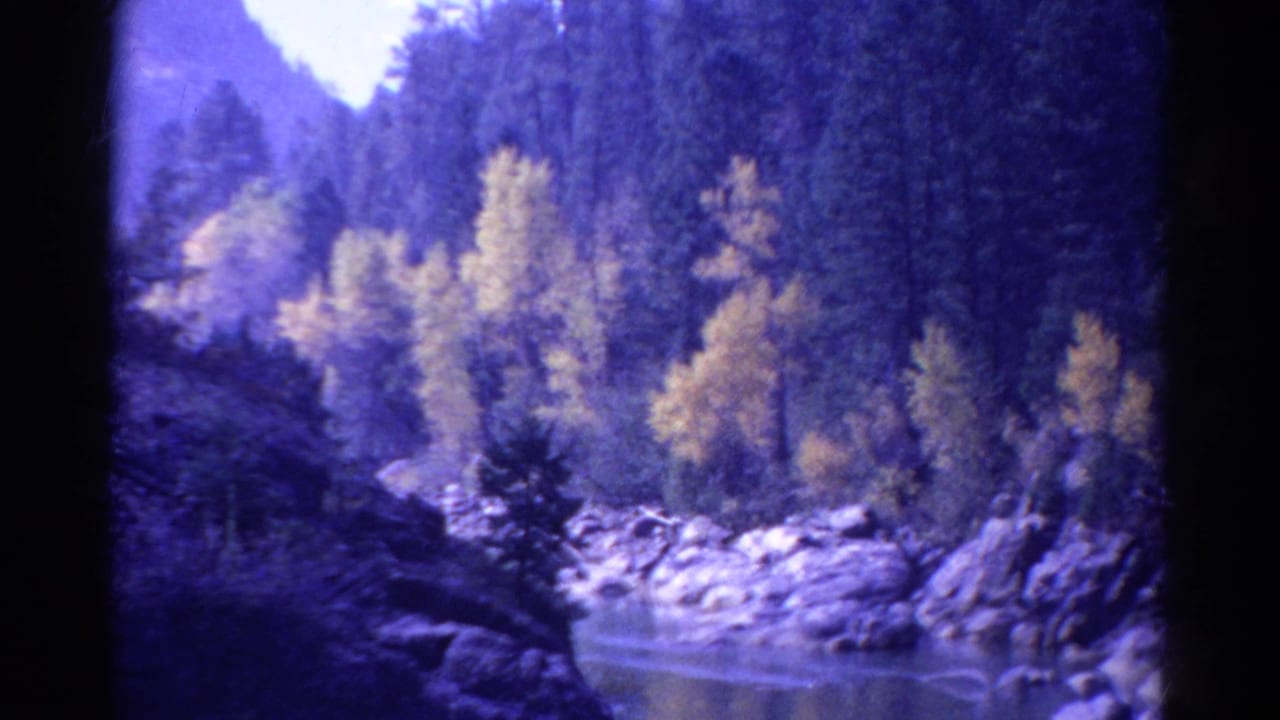 Mountain river bend with rocks, yellow trees, evergreens, and dark film edges.
