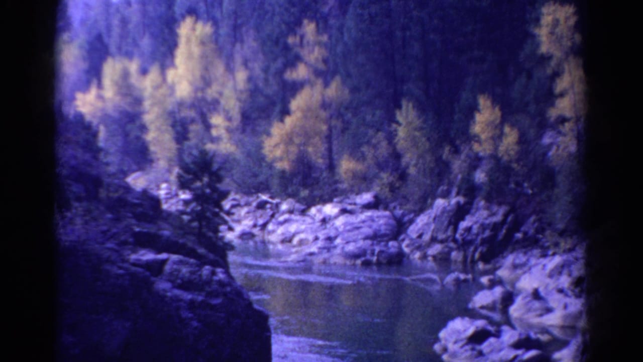 1967 Colorado 8mm frame showing a river bend below rocky slopes, evergreen trees, and autumn-yellow foliage.