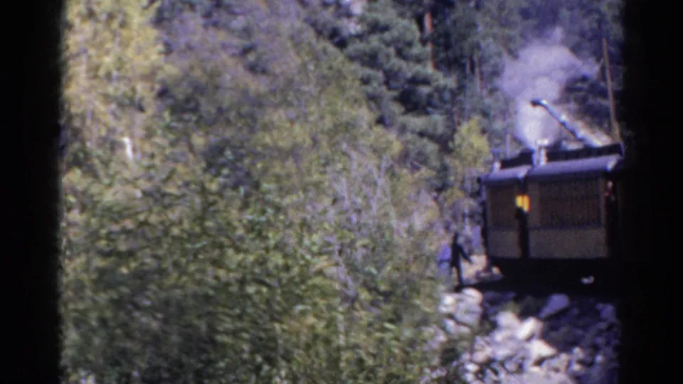 1967 Colorado 8mm frame showing a steam train rounding through dense trees and rocks in a mountain canyon.