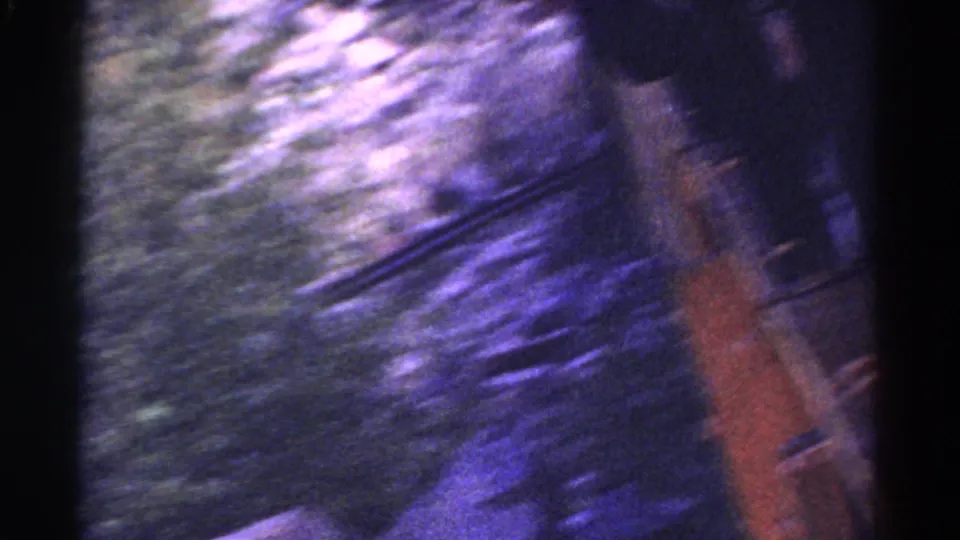 A heavily blurred 1967 Colorado 8mm frame shows trackside greenery and the edge of the moving train with strong blue-purple film shift.