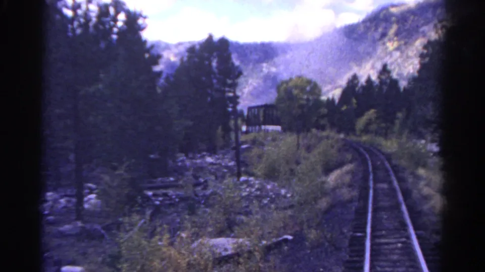 1967 Colorado 8mm frame looking down a curving rail line through pine trees and rocky mountain terrain.
