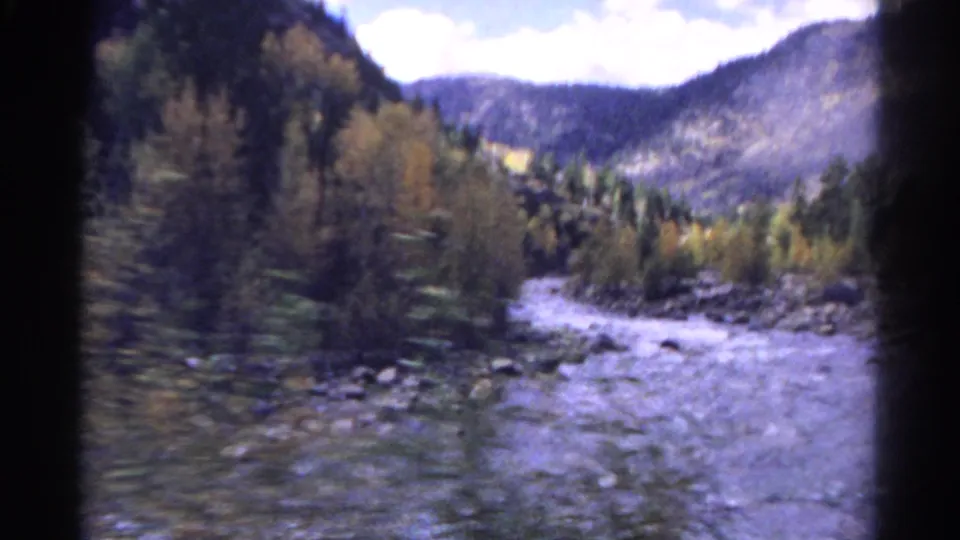 1967 Colorado train-view frame showing a rocky river, autumn-colored trees, forest, and mountain valley.