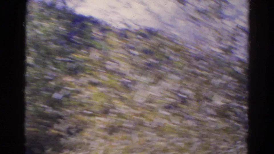 Motion-blurred 1967 Colorado 8mm frame showing brush, hillside vegetation, and the moving camera's handheld travel perspective.