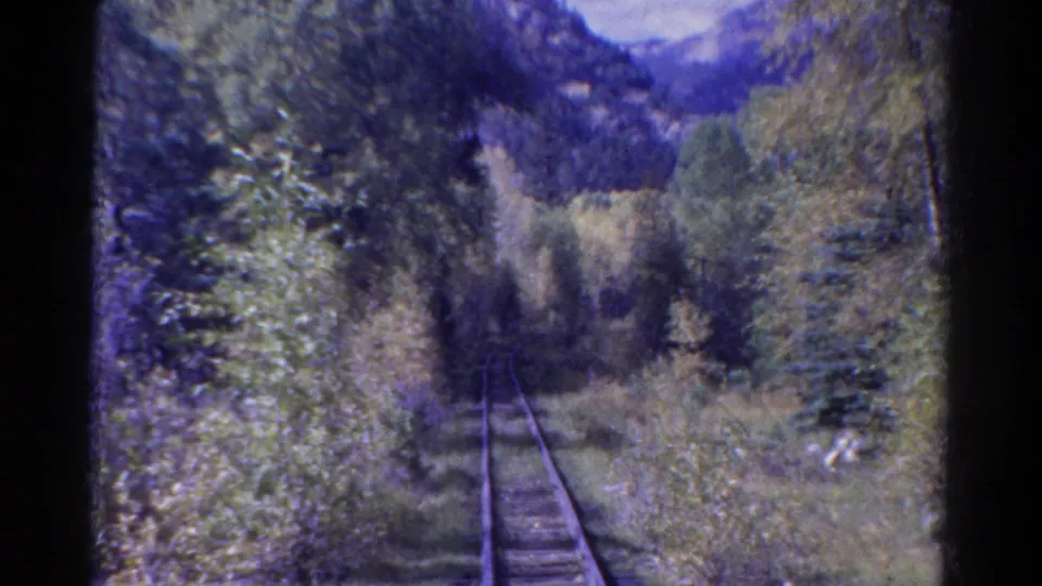 8mm home-movie frame of Colorado tracks passing through dense vegetation, framed by dark film edges and soft color shift.