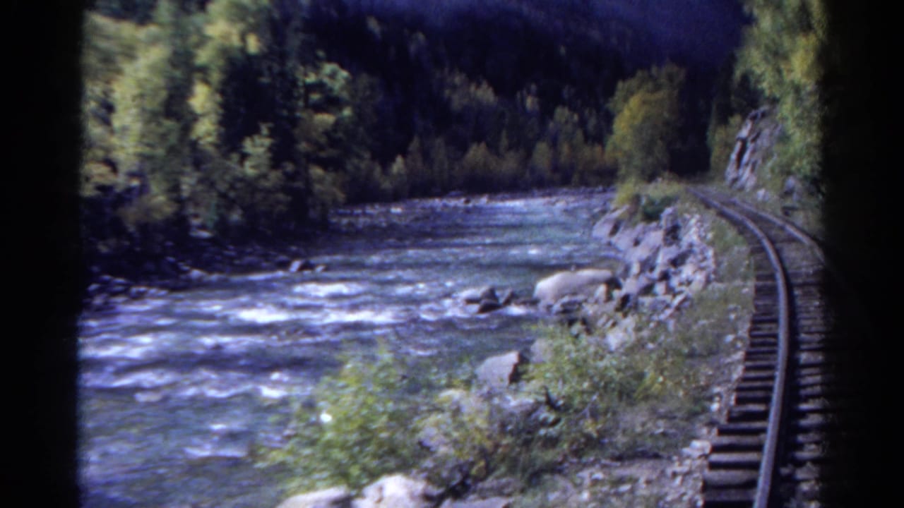 1967 Colorado 8mm frame showing a rushing river, rocky bank, trees, and rail tracks curving along the water.