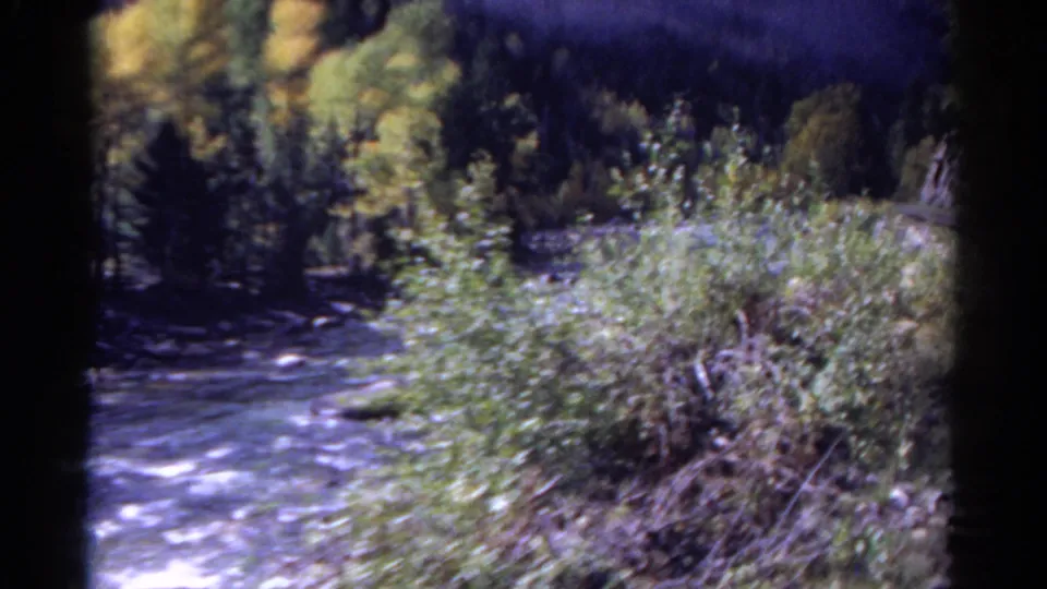 1967 Colorado 8mm frame showing a river bend, dense brush, rocky bank, and train tracks running along the woods.