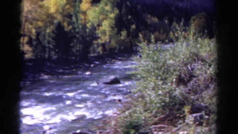 1967 Colorado 8mm home-movie view of a fast river with whitewater, rocks, brush, and trees along the bank.