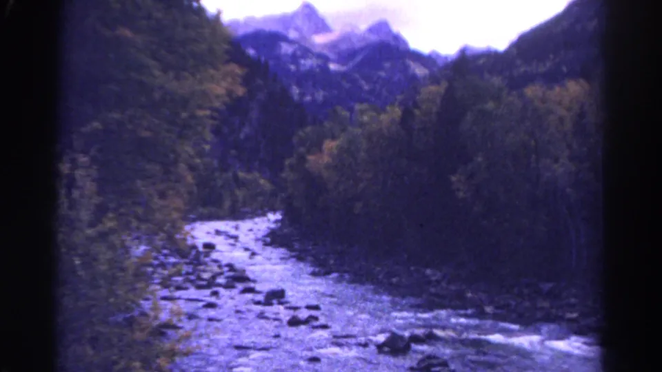 1967 Colorado 8mm view of a rocky creek winding through forest toward distant mountain peaks.