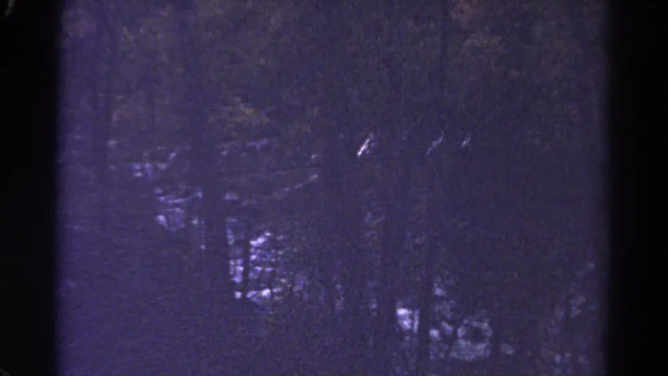 1967 Colorado 8mm frame showing a dark forested river with small bright rapids and soft, grainy detail.