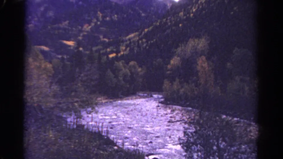 1967 Colorado 8mm frame showing a wide river bend, dense trees, rocky shoreline, and forested slopes under soft vintage color.