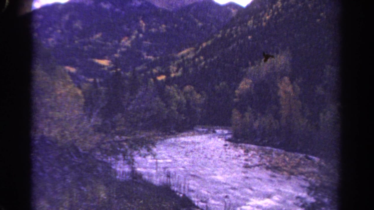 Rushing river curving through a wooded mountain valley with dark film borders.