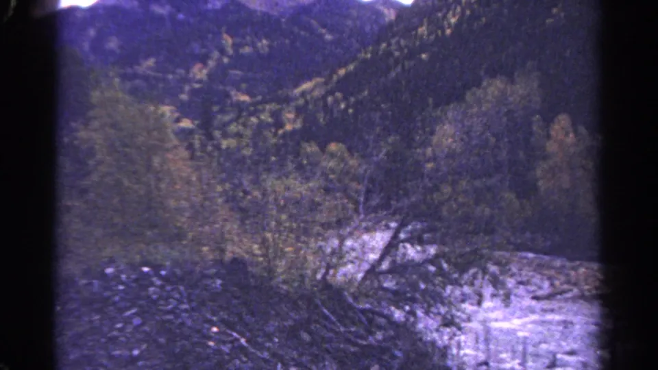 1967 Colorado home-movie frame of bright river water, nearby trees, and dark wooded mountain slopes.