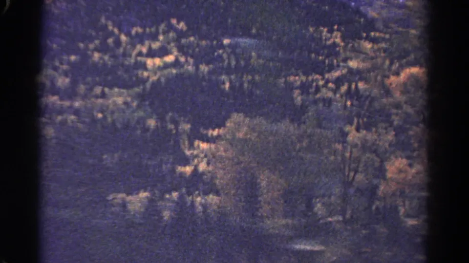 1967 Colorado 8mm frame of wooded terrain with bright tree patches and a central dark frame boundary.