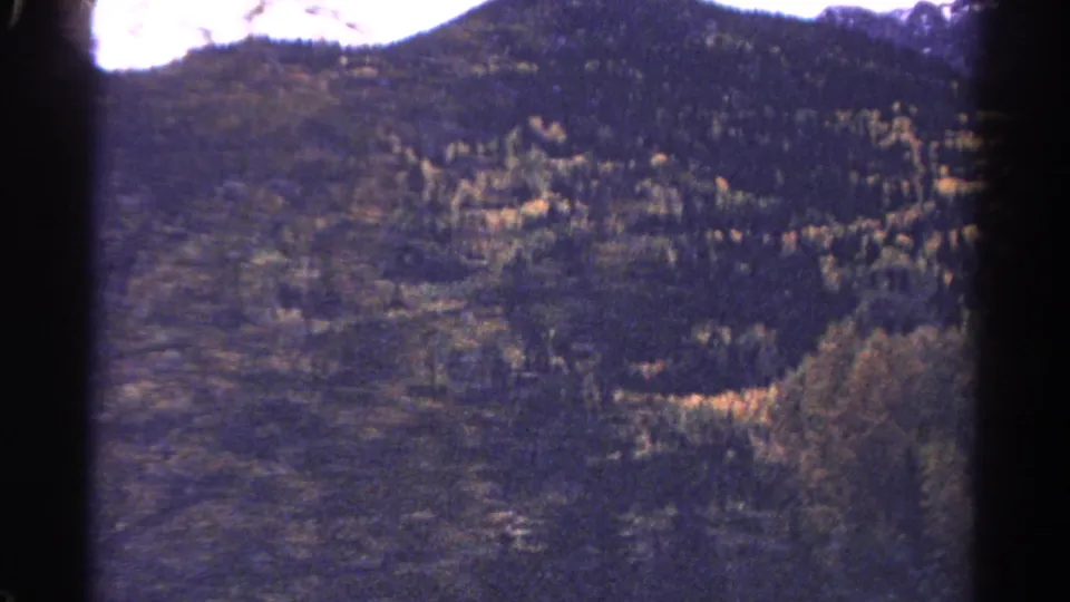1967 Colorado 8mm frame with wooded hills, a distant ridge, bright sky, and visible film-edge shadow.