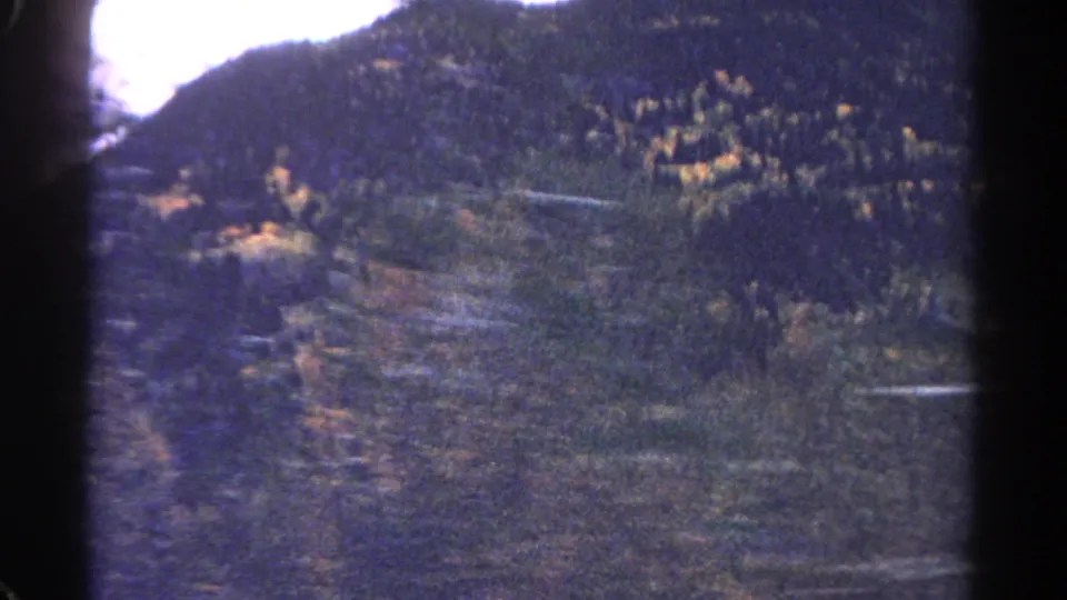 1967 Colorado 8mm frame showing a soft, grainy view of forested hills and valley contours during a roadside drive.