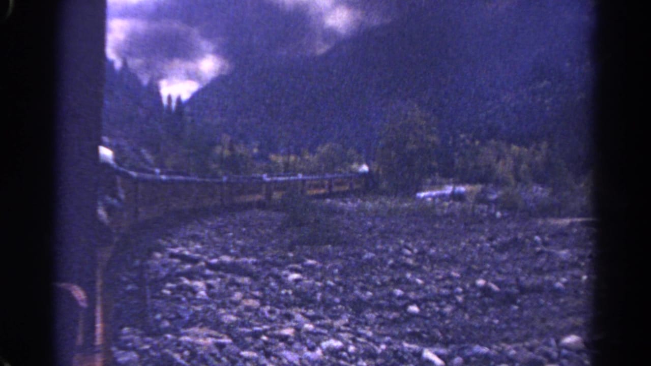 Mountain rail scene with rocky foreground, trees, and low cloud.