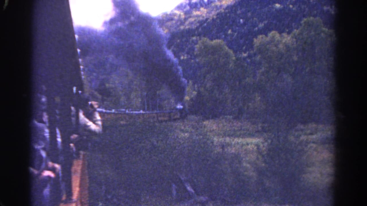 Steam train edge with smoke drifting over a wooded hillside.