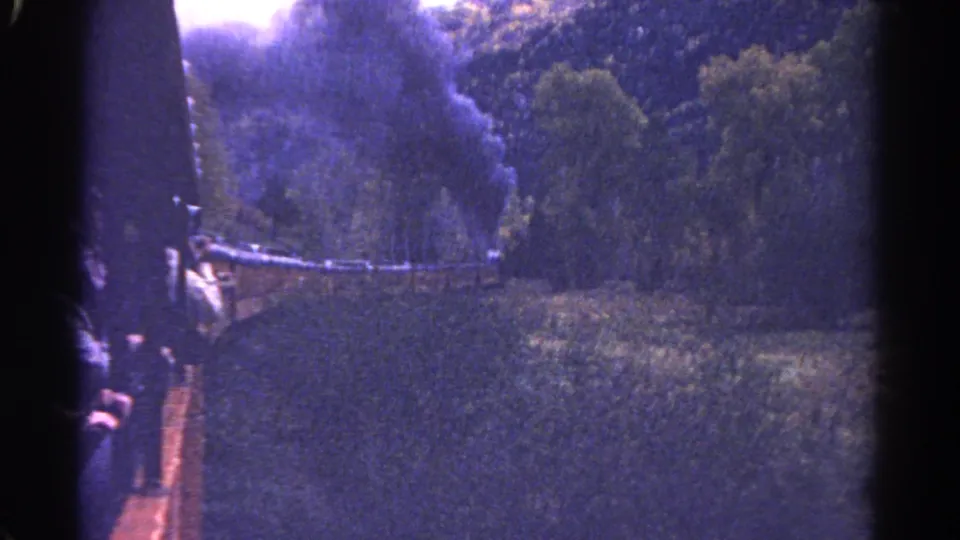 Purple-cast 8mm frame from Colorado showing a steam train car, smoke, and dense forest in 1967.