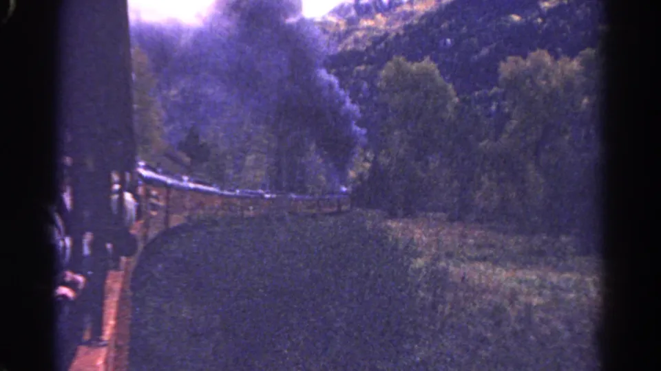 1967 Colorado 8mm still with a steam train at frame edge, passengers, smoke, and forested hills.