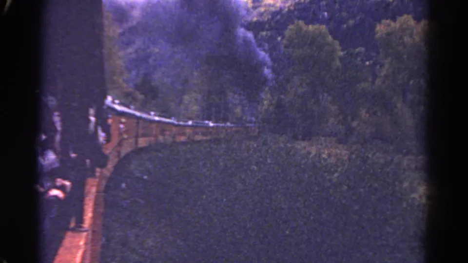 Colorado home-movie frame from 1967 showing a steam train moving through woodland, seen from a passenger perspective beside dark frame edges.