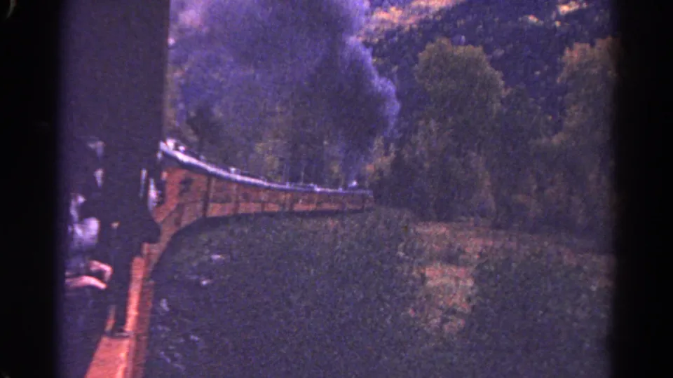 1967 Colorado travel frame showing a steam train on a wooded curve, with smoke drifting upward and a passenger-side view along the cars.