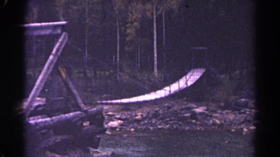 1967 Colorado home-movie frame of a rustic bridge and rocky creek in a wooded setting.