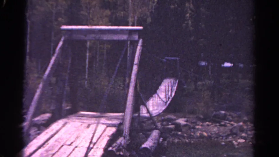 1967 Colorado 8mm view from near the bridge approach, with pale planks, timber frame and dark deciduous forest beyond.