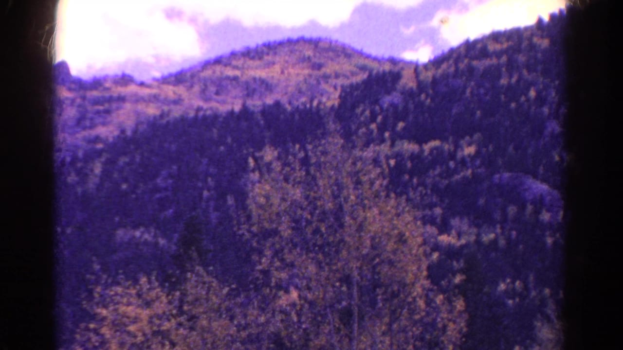 Forested mountain slope beneath bright clouds with dark 8mm frame edges.