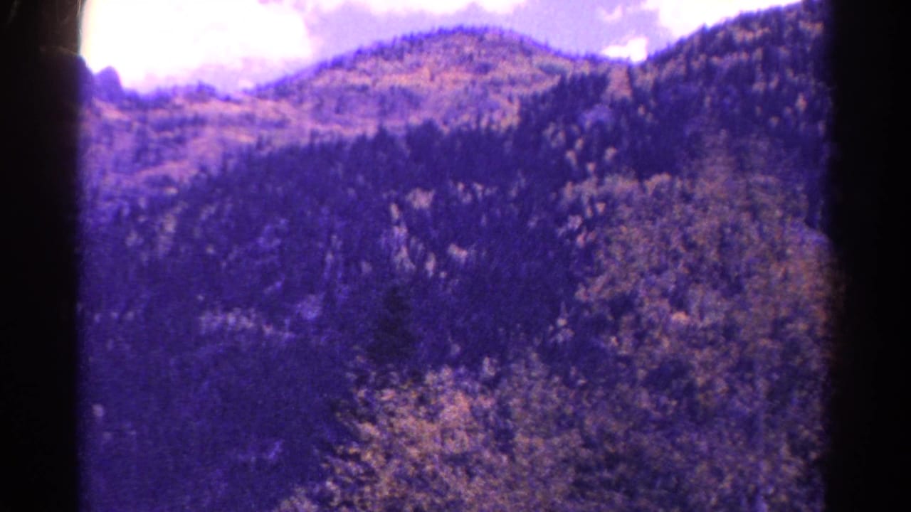 Tree-covered mountain ridge and cloudy sky with dark vertical film border.