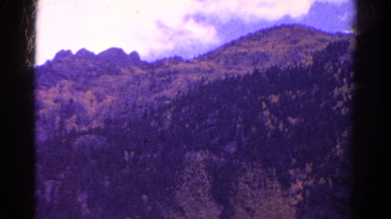 Forested mountain slope and rocky ridge seen through aged film borders.