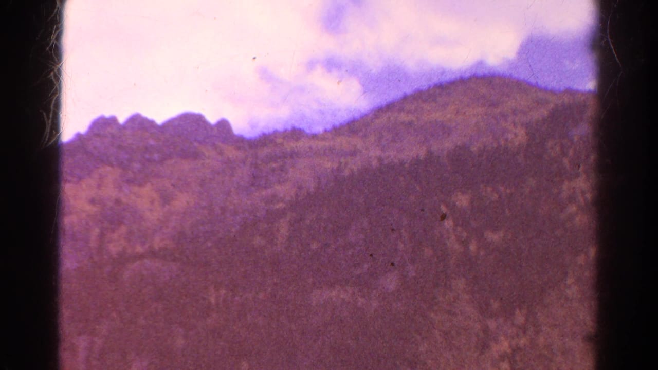 1967 Colorado mountain view with wooded slopes, rounded ridge forms, cloudy sky, and visible aged-film color fading.