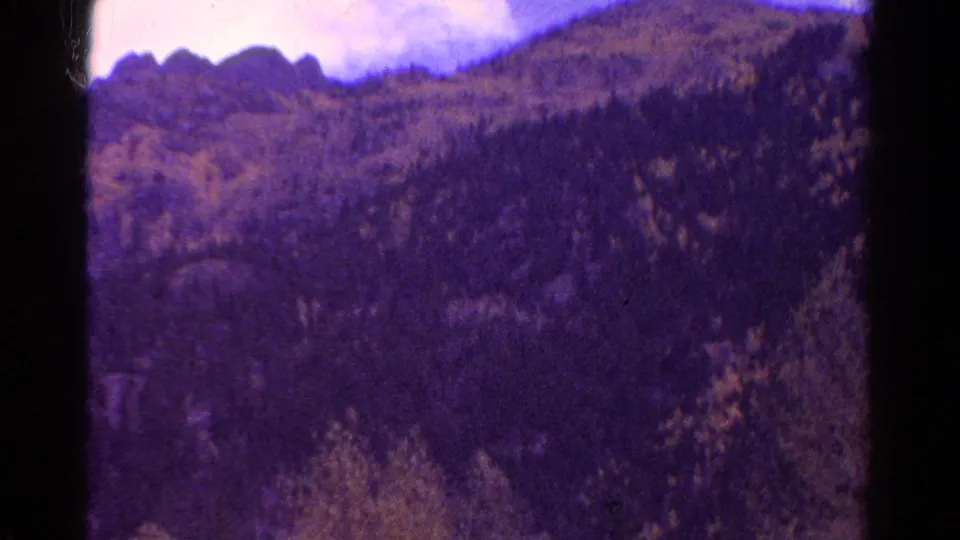 1967 Colorado 8mm view of a forested mountain slope and rocky ridge, blurred by vehicle motion and aged film texture.