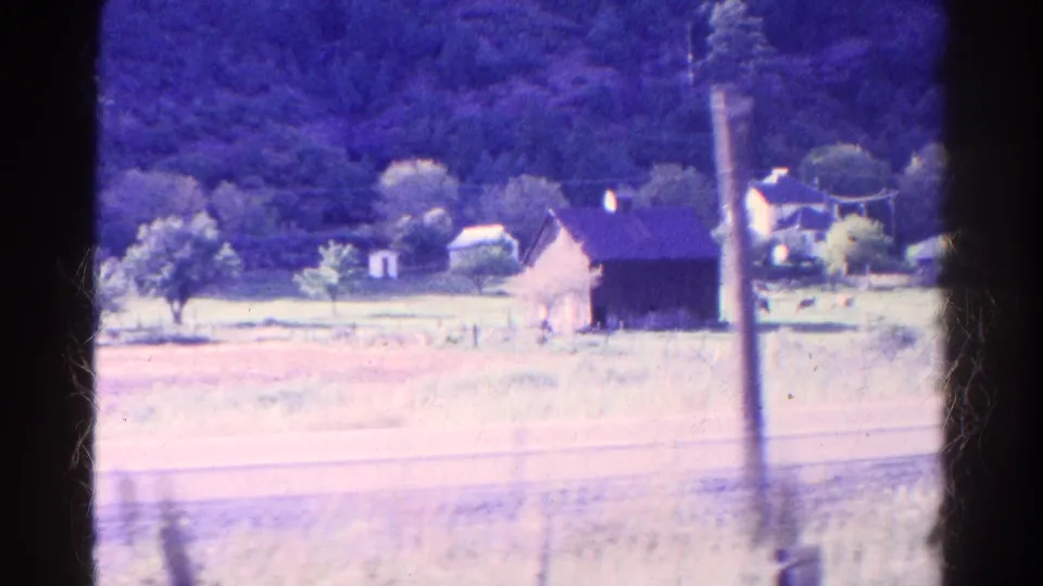 1967 Colorado train view showing a rural barn and house, trees, pasture fencing, hillside, and a blurred pole passing in the foreground.