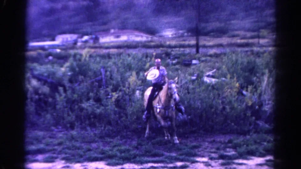 1967 Colorado 8mm frame with a horseback rider holding or wearing a pale hat in a brushy rural landscape.