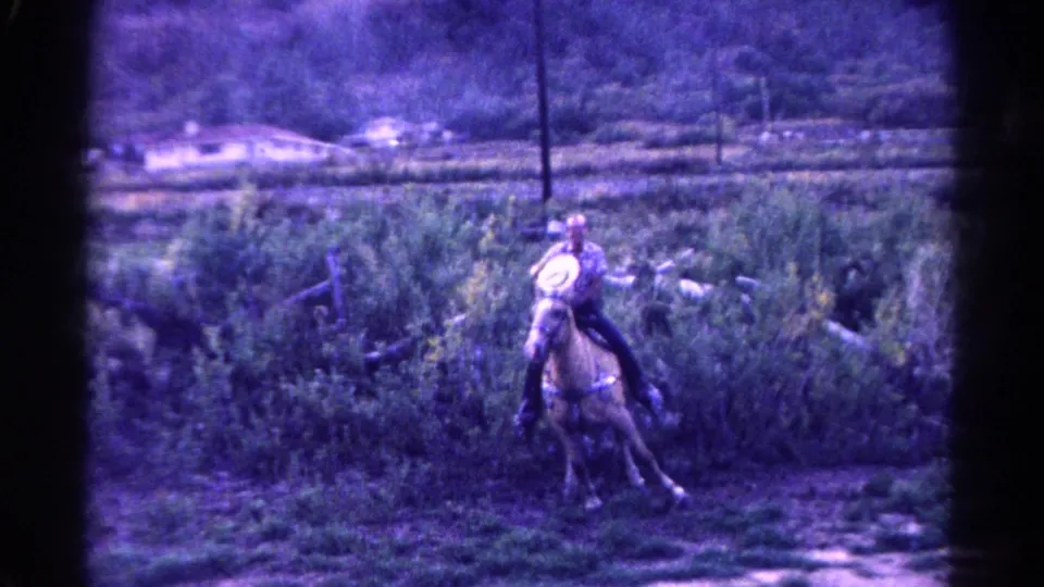 1967 Colorado 8mm frame of an adult rider in a cowboy hat guiding a palomino horse through a brushy field.