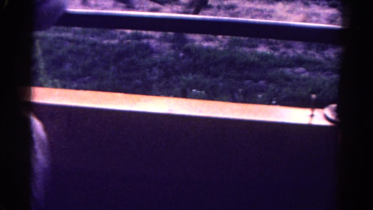 Home-movie view from inside or beside a vehicle, looking past dark window framing toward scrubby roadside ground in Colorado.