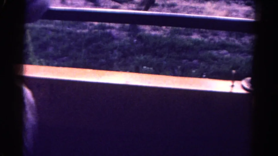 Home-movie view from inside or beside a vehicle, looking past dark window framing toward scrubby roadside ground in Colorado.