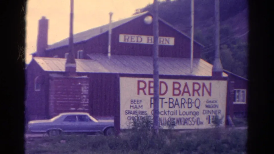 1967 Colorado frame showing the Red Barn Pit-Bar-B-Q building, a large roadside menu sign, utility poles, and a parked light-colored car.
