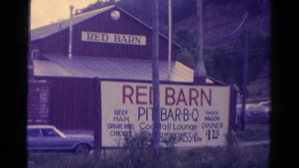 Closer 1967 Colorado view of the Red Barn Pit-Bar-B-Q facade and large sign advertising meats, lounge, and dinner specials.