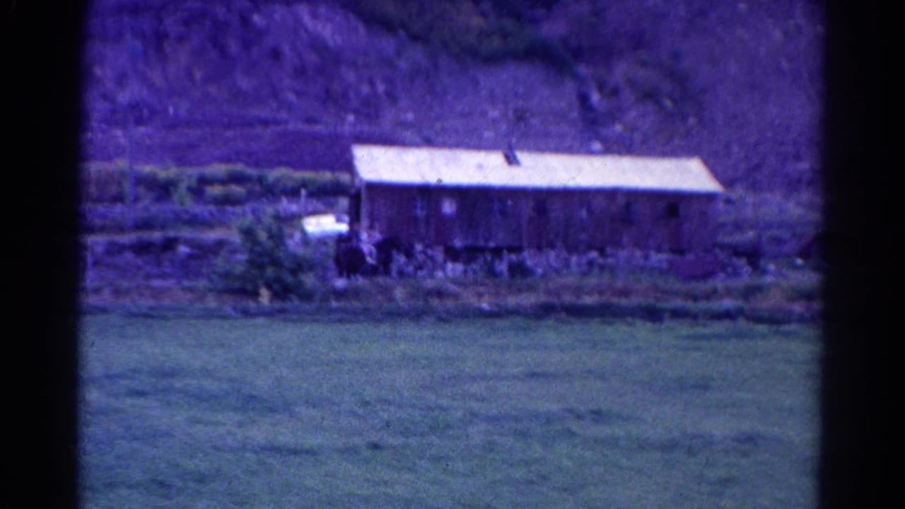 Wooden farm structure with pasture in front and hillside behind.