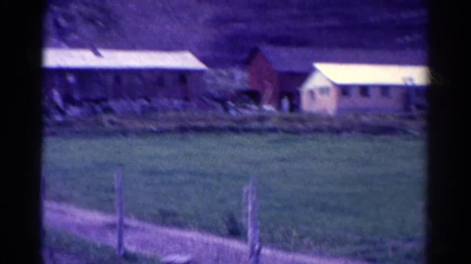 The final 1967 Colorado frame shows pasture, wire fence posts, a long farm building, smaller outbuildings, and hillside beyond.