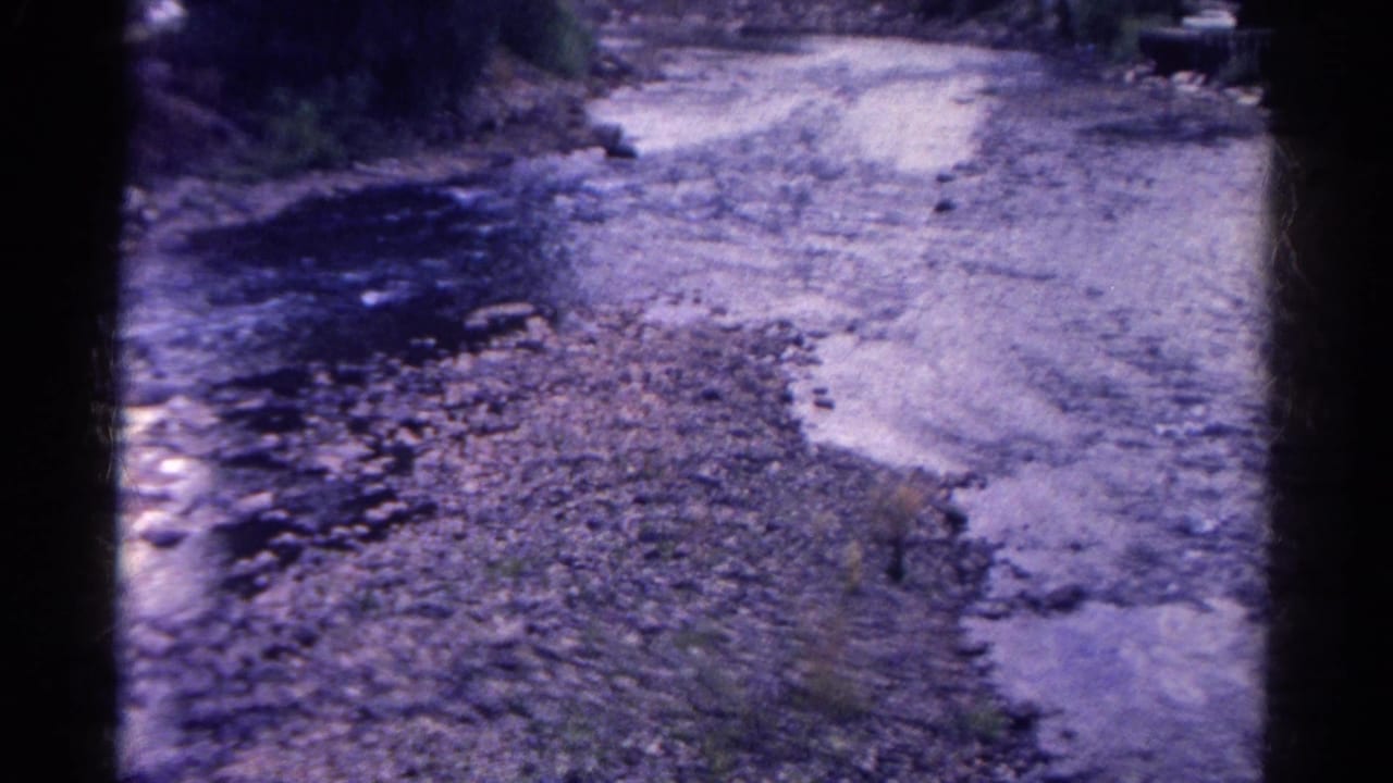 Rocky streambed beside a dirt road or bank, with shallow water running through the frame.