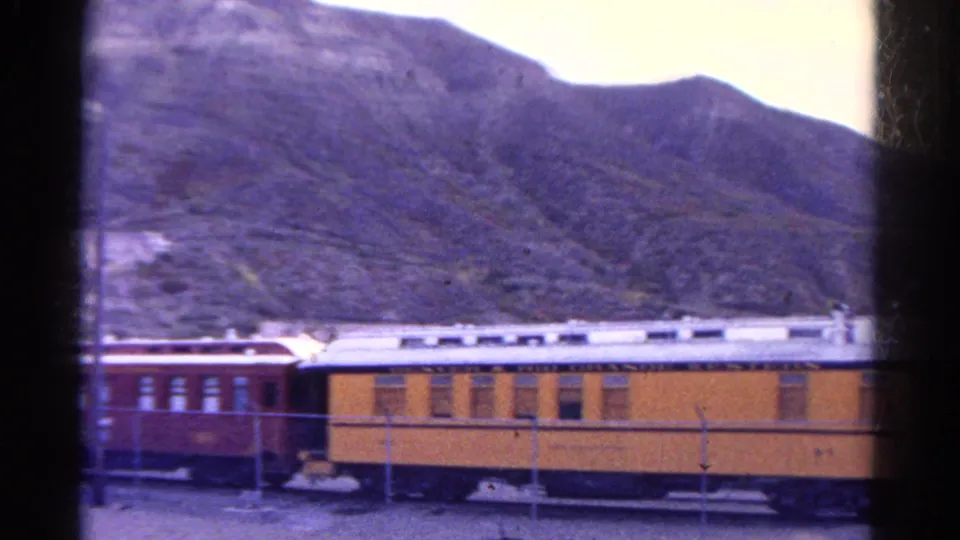 1967 Colorado train-window view of yellow and red passenger rail cars passing along a rocky mountain slope.