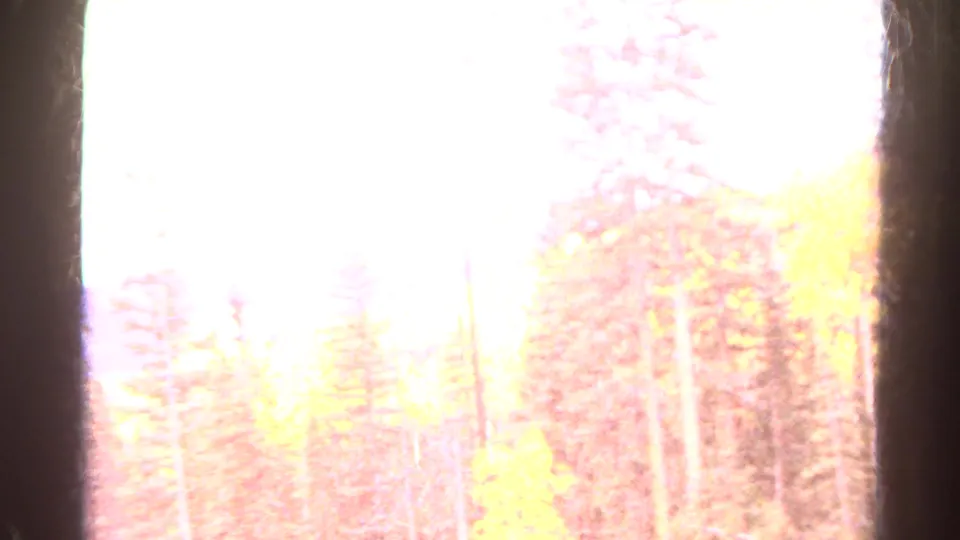 Overexposed Colorado mountain landscape frame with a pale sky, faint trees, and dark vertical film or window-like borders.