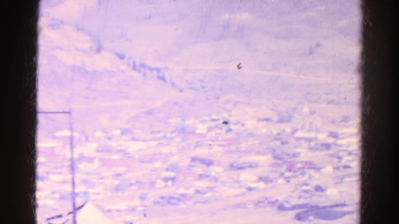 1967 Colorado 8mm view of a small mountain town in a valley, framed by dark window edges and aged purple color.